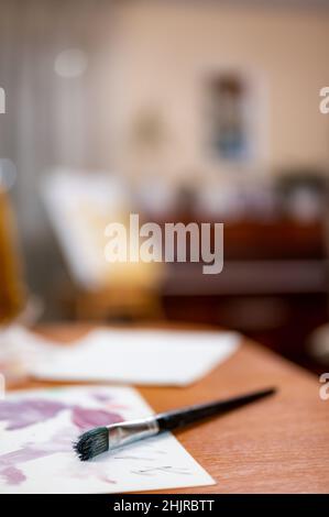 Le pinceau large repose sur du papier sur une table en bois avec un arrière-plan intérieur flou Banque D'Images