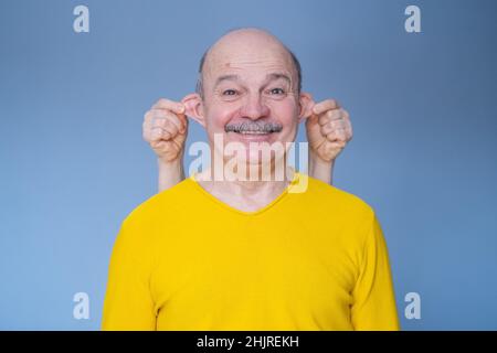 Drôle caucasien lop élevé homme dans le chandail jaune souriant sur le mur bleu. Banque D'Images