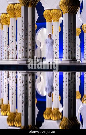 Abu Dhabi, Émirats Arabes Unis - 03 2021 décembre : portrait de réflexion sur l'eau d'un jeune homme blanc en robe arabe traditionnelle dans la colonnade de la Grande Mosquée de Zayed Banque D'Images