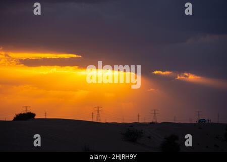 Coucher de soleil spectaculaire dans le désert, le soleil sort des nuages sombres, avec une ligne électrique en arrière-plan, Dubaï, Émirats Arabes Unis Banque D'Images