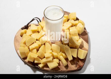 Concept de lait de pomme de terre.Lait de remplacement.Un verre de lait sur une planche de bois avec des pommes de terre crues hachées. Banque D'Images