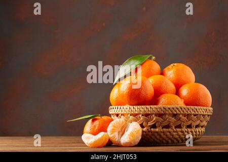 Сlementine mandarines avec feuilles dans un panier en bois sur fond sombre avec espace de copie Banque D'Images