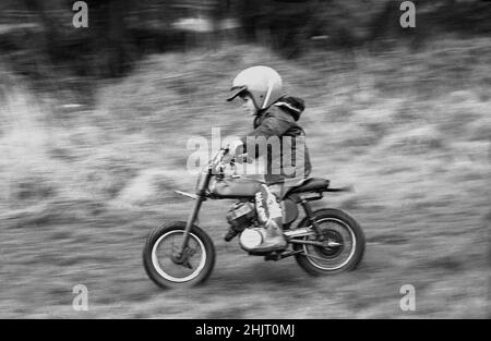 1970s, historique, à l'extérieur sur une piste boueuse, un petit garçon portant une veste et un casque de sécurité à bord d'une mini moto de brouille, Angleterre, Royaume-Uni.Également connu sous le nom de mini-brouilleurs ou de mini-motos de terre, ainsi que d'avoir l'amusement de la conduite sur terrain accidenté, les cavaliers âgés de 6 à 9 ans peuvent également prendre part à des courses organisées de mini moto. Banque D'Images