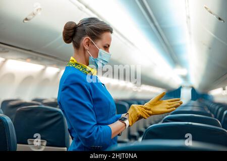 Hôtesse dans un masque médical mettant des gants dans un avion Banque D'Images