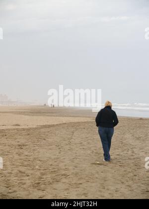 Une personne seule marchant le long de la plage vide dans le brouillard Banque D'Images
