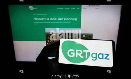 Personne tenant un téléphone portable avec le logo de la société française de gaz naturel GRTgaz sa à l'écran en face de la page web d'affaires.Mise au point sur l'affichage du téléphone. Banque D'Images