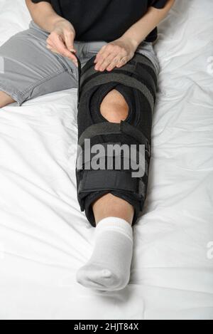 Femme fixant l'orthèse de Velcro réglable sur une jambe cassée assise dans le lit.Port d'une jambe de force après une blessure.Gros plan.Orientation verticale Banque D'Images