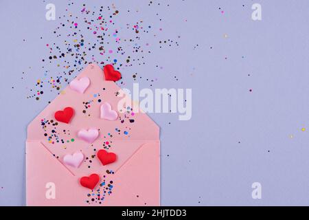 Saint-Valentin fond de fête.Enveloppe rose avec coeurs rouges et confettis sur fond violet tendance avec espace de copie.Flat lay, vue de dessus Banque D'Images