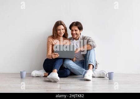 Un jeune couple européen souriant assis sur le sol, se reposant d'un déménagement à la maison, à la recherche d'une idée de nouvel intérieur Banque D'Images