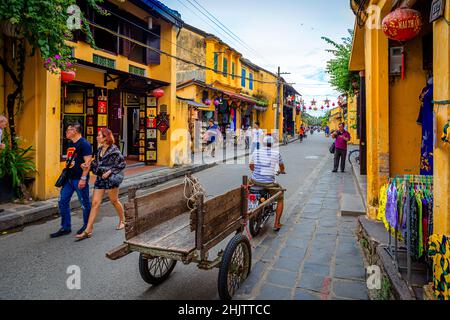 Une ancienne voiturette traditionnelle tirée par une moto se trouve au milieu de la rue de la vieille ville de Hoi an avec quelques boutiques de touristes. Banque D'Images