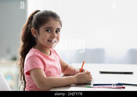 Belle petite fille en piquant à la table et dessin avec des crayons colorés Banque D'Images