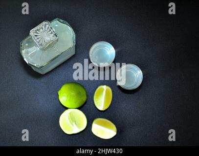 Une bouteille et deux verres de tequila et de sel sur fond noir, à côté des limbes coupés.Vue de dessus, plan d'appartement. Banque D'Images