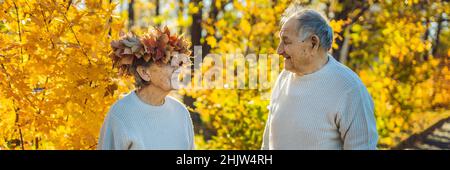 Vieux couple heureux s'amuser au parc d'automne. Un homme âgé portant une couronne de feuilles d'automne à sa vieille épouse BANNER, format long Banque D'Images