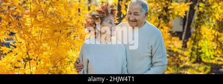 Vieux couple heureux s'amuser au parc d'automne. Un homme âgé portant une couronne de feuilles d'automne à sa vieille épouse BANNER, format long Banque D'Images