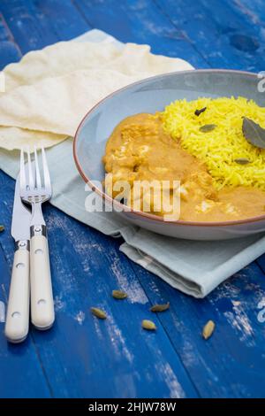 Gros plan du korma de poulet alimentaire indien cuit avec du riz pilau et des graines de cardamome sur une table en bois Banque D'Images