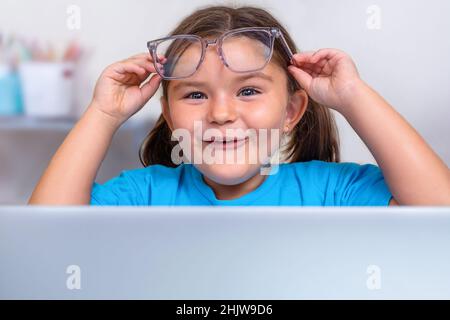 Portrait de l'enfant dans des lunettes de vue piquant dans la surprise de derrière un ordinateur portable Banque D'Images