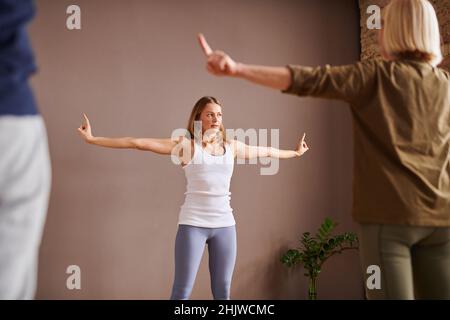 Jeune instructeur de fitness montrant les exercices d'étirement à sa classe de personnes âgées pendant l'entraînement sportif dans le club de santé Banque D'Images