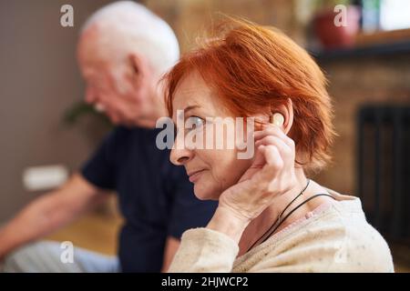 Vue latérale d'une femme âgée aux cheveux rouges courts à l'aide de son aide auditive lorsqu'elle est assise avec d'autres personnes en cours de yoga Banque D'Images