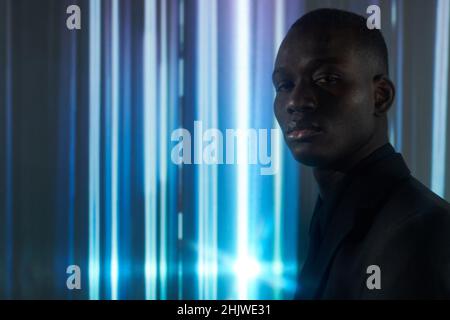 Jeune homme d'affaires sérieux en tenue noire sur fond rayé et regardant l'appareil photo Banque D'Images