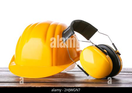 Casque de sécurité et cache-oreilles sur table en bois sur fond blanc Banque D'Images