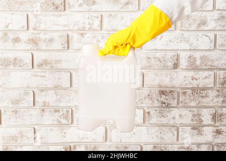 Main mâle dans des gants en caoutchouc tenant le contenant près du mur de briques Banque D'Images