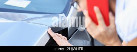 Une femme pilote parle sur un smartphone et examine les dommages causés à la voiture après un accident de proximité Banque D'Images