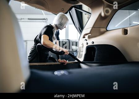 Femme travailleuse aspirant poussière intérieur de la voiture dans le lave-auto. Banque D'Images
