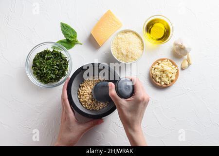 Pesto sauce cuisson avec les mains de la femme et le mortier .Basilic, huile d'olive, parmesan, ail, pignons.Vue de dessus avec espace table en pierre blanche pour votre texte t Banque D'Images