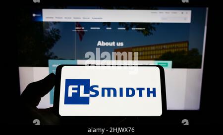 Personne tenant un téléphone portable avec le logo de l'ingénierie danoise FLSmidth Co. COMME sur l'écran en face de la page Web d'affaires.Mise au point sur l'affichage du téléphone. Banque D'Images