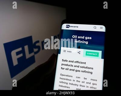 Personne tenant un téléphone portable avec la page web de l'ingénierie danoise FLSMIDth Co. COMME à l'écran devant le logo de l'entreprise.Mise au point sur l'affichage du téléphone. Banque D'Images
