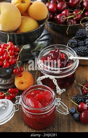 Pots de confiture de fraises de cerise parmi les fruits d'été et d'automne sur une table en bois. Banque D'Images