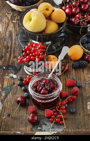 Pots de confiture de fraises de cerise parmi les fruits d'été et d'automne sur une table en bois. Banque D'Images