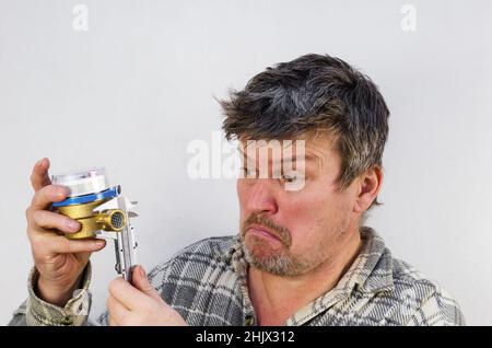 Le visage surpris d'un homme mesurant un compteur d'eau avec un pied à coulisse.L'homme tient le compteur d'eau et la jauge dans ses mains.Un homme avec emmêlé, dis Banque D'Images