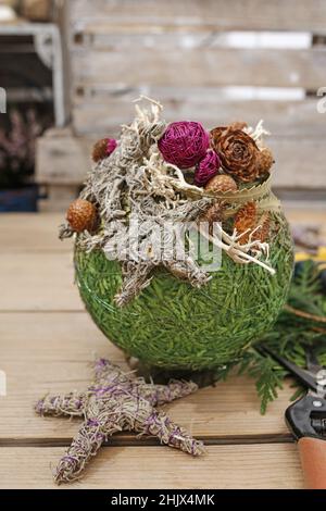 Fleuriste au travail: Femme montre comment faire boule de Noël avec sphère de styromousse et brindilles de thuja. Étape par étape, tutoriel. Banque D'Images