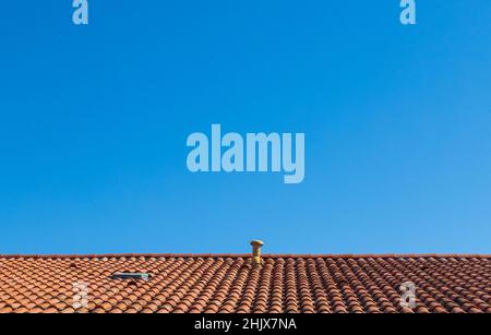 Sur fond de ciel bleu clair, un toit orange contrasté fait de vieux carreaux Banque D'Images