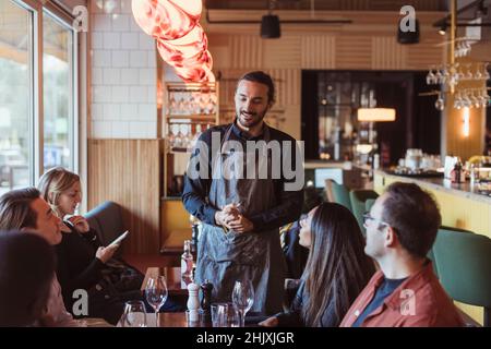 Clients multiraciaux qui commandent de la nourriture auprès d'un serveur au restaurant Banque D'Images