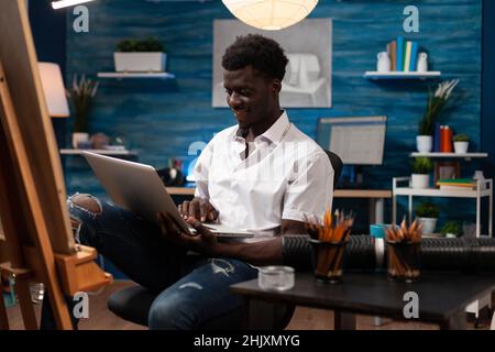 Jeune artiste tenant un ordinateur portable à la recherche de l'inspiration de dessiner tout en travaillant à chef-d'œuvre artistique dans studio d'art à la maison. illustrator homme esquissant un vase sur toile à l'aide d'un crayon graphique professionnel Banque D'Images