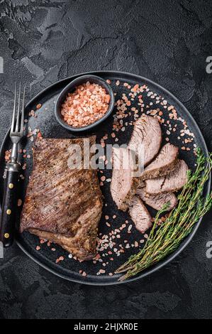 Griller un steak de bœuf Wagyu vieilli tri Tip sur une assiette de sel rose.Arrière-plan noir.Vue de dessus Banque D'Images