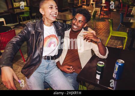 Deux meilleurs amis rient avec joie dans un restaurant en plein air.Deux jeunes joyeux ayant des bières ensemble la nuit.Amis qui ont un bon moment Banque D'Images