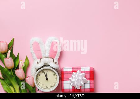 Carte de Pâques.Réveil avec des oreilles de lapin cadeau fleurs tulipes sur fond rose.Vue de dessus de l'espace de copie de la mise à plat Banque D'Images