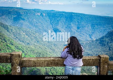 une jeune fille qui regarde la chaîne de montagnes avec un ciel bleu vif l'après-midi à partir d'une image d'angle plat est prise à la chute d'eau de sept sœurs cherrapunji meghalay Banque D'Images