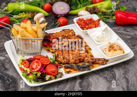 Cuisse de poulet grillée sur une assiette en porcelaine blanche avec frites et salade Banque D'Images