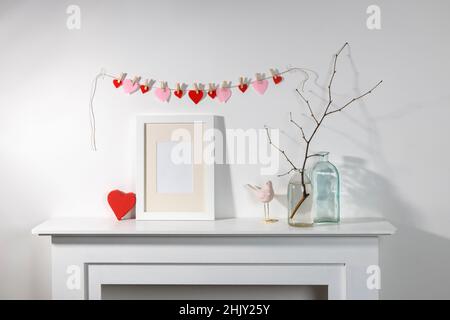 Décoration pour la Saint-Valentin.Une guirlande de coeurs en feutre sur une cheminée décorative.Cadre photo, un vase avec une branche, un cadeau dans une boîte en forme de coeur, Banque D'Images