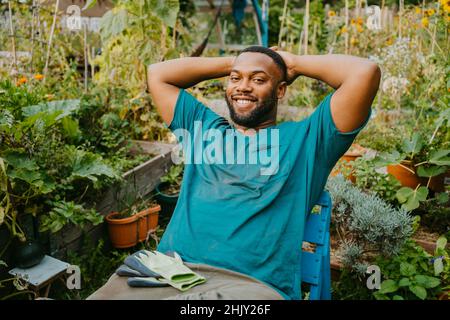 Portrait d'un homme bénévole souriant avec les mains derrière la tête assis dans le jardin communautaire Banque D'Images