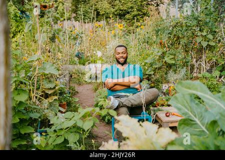 Portrait d'un fermier souriant avec les bras croisés assis dans le jardin communautaire Banque D'Images