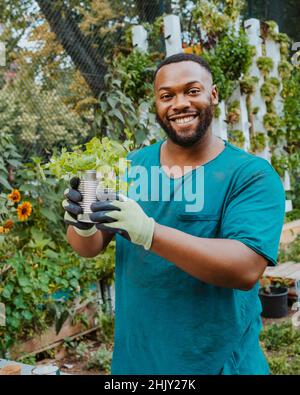 Portrait d'un homme souriant volontaire tenant une plante en pot dans le jardin de la communauté Banque D'Images