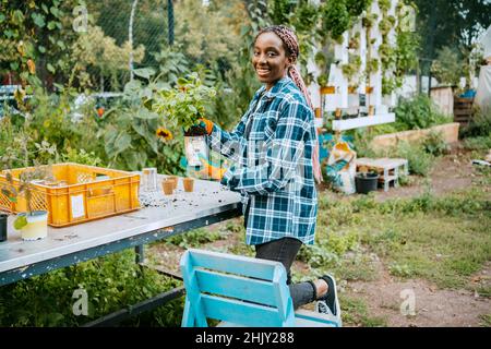 Portrait d'une agricultrice souriante avec plante en pot dans le jardin de la communauté Banque D'Images