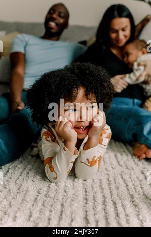 Fille souriante avec la tête dans les mains couchée sur le tapis à la maison Banque D'Images