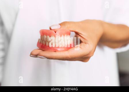 Prothèse dentaire dans les mains du médecin en gros plan.Dentiste tenant un pont dentaire en céramique.Vue avant de la prothèse complète.Pho conceptuel de la dentisterie Banque D'Images
