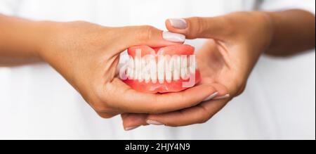 Prothèse dentaire dans les mains du médecin en gros plan.Dentiste tenant un pont dentaire en céramique.Vue avant de la prothèse complète.Pho conceptuel de la dentisterie Banque D'Images